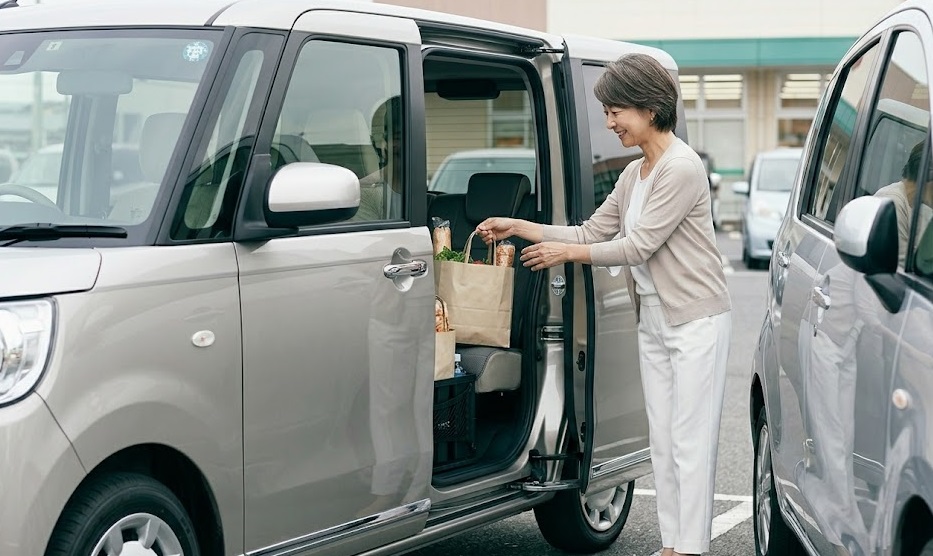 狭い駐車場で、隣の車に気兼ねなく両側スライドドアを開け、荷物を積み込む大人の日本人女性。ムーヴキャンバスの絶妙な車高と利便性を表現